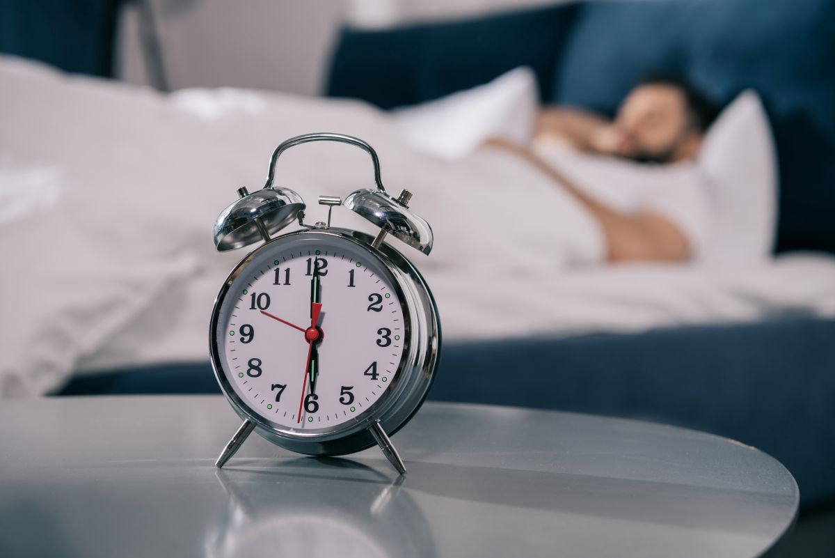 un homme allongé dans son lit avec un réveil en premier plan